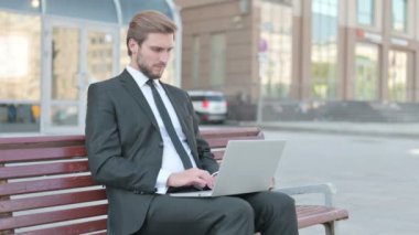 Busy Middle Aged Businessman Using Laptop Sitting Outdoor on Bench