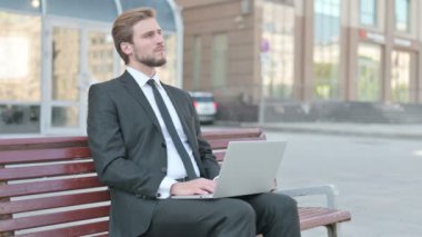 Thinking Middle Aged Businessman Using Laptop while Sitting Outdoor on Bench