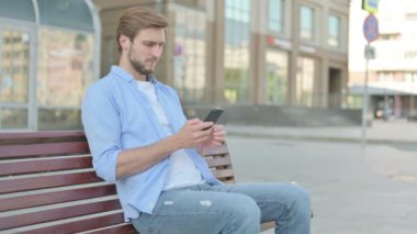 Orta Çağ Adamı Smartphone 'da internette gezinirken Bench' in dışında oturuyor.