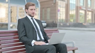 Middle Aged Businessman Talking on Video Call while Sitting Outdoor on Bench