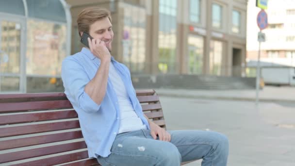 Mann Mittleren Alters Telefoniert Während Draußen Auf Bank Sitzt — Stockvideo