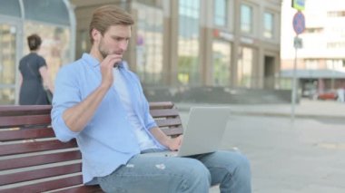 Boyun Ağrısı olan orta yaşlı bir adam Bench 'te otururken dizüstü bilgisayar kullanıyor.
