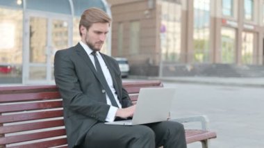 Middle Aged Businessman with Laptop Smiling at Camera while Sitting Outdoor on Bench