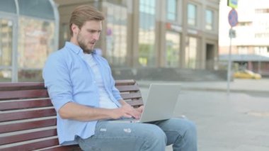 Orta yaşlı adam Bench 'te otururken dizüstü bilgisayar kullanıyor.