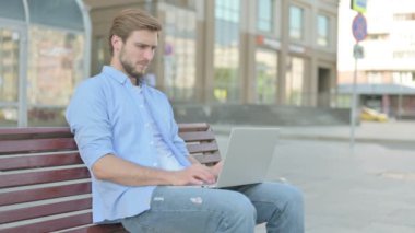 Sırt ağrısı olan orta yaşlı bir adam Bench 'te otururken dizüstü bilgisayar kullanıyor.