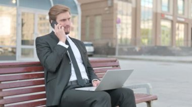 Angry Businessman with Laptop Talking on Phone, Sitting Outdoor on Bench