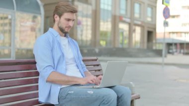 Man Pointing at the Camera while Sitting on Bench Outdoor
