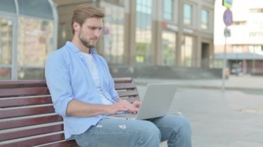 Bilek ağrısı olan adam Bench 'te otururken dizüstü bilgisayar kullanıyor.
