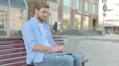 Thumbs Down by Man with Laptop Sitting on Bench 