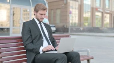 Thumbs Down by Businessman with Laptop Sitting on Bench 