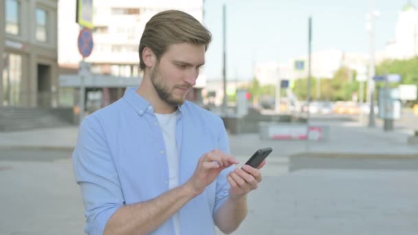 スマートフォンの屋外でオンライン成功を祝う中年男性 — ストック動画