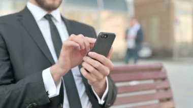 Middle Aged Businessman Browsing Internet on Smartphone while Sitting Outdoor on Bench