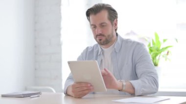 Mature Man Celebrating Success on Tablet in Office 