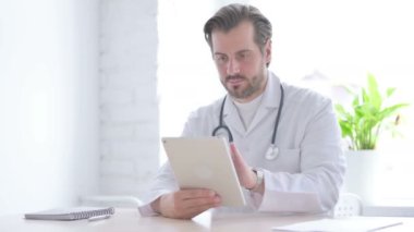 Male Doctor using Tablet while Sitting in Clinic