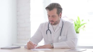 Male Doctor Writing on Paper in Clinic, Medical Report