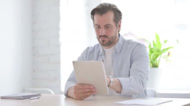 Mature Man using Tablet while Sitting in Office