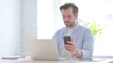 Mature Man using Smartphone while using Laptop 