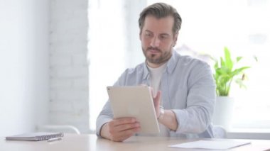 Mature Man Reacting to Loss on Tablet in Office 