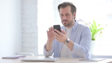 Successful Mature Man Celebrating on Smartphone in Office 