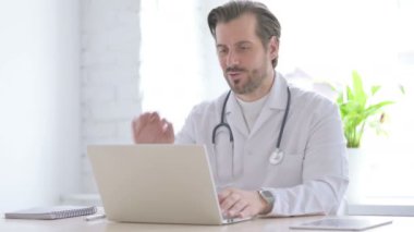 Male Doctor Talking on Video Call on Laptop in Clinic