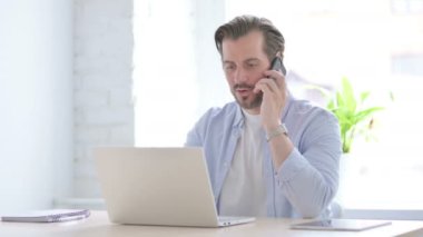 Mature Man Talking on Phone while using Laptop