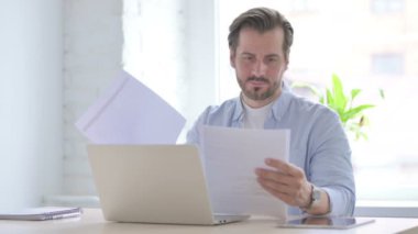 Mature Man Doing Paperwork on Laptop in Office