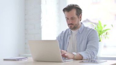 Mature Man Looking at Camera while using Laptop