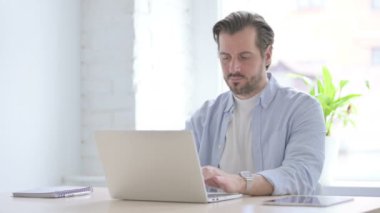 Mature Man Smiling at Camera while using Laptop