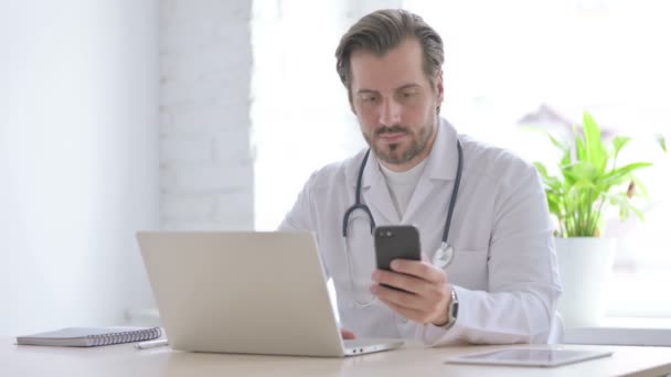 Male Doctor Using Smartphone While Using Laptop Clinic — Vídeo de stock