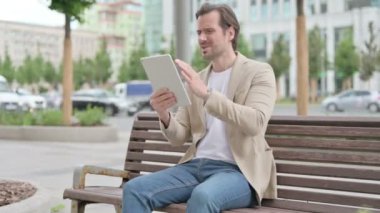 Upset Man Reacting to Loss on Tablet while Sitting on Bench