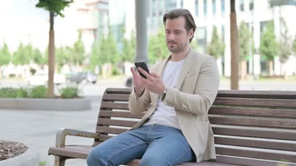 Man Celebrating Online Success Smartphone While Sitting Bench — Stockvideo