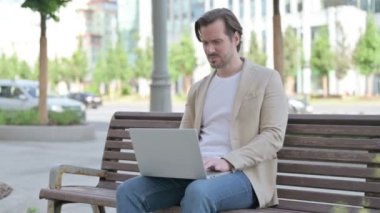 Man Reacting to Loss on Laptop while Sitting on Bench