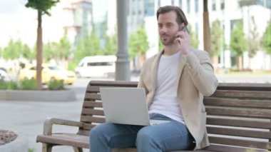 Man Talking on Phone and using Laptop while Sitting on Bench