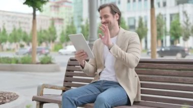 Online Video Chat on Tablet by Man Sitting on Bench 