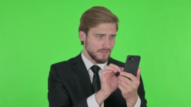 Young Adult Businessman Loss on Smartphone on Green Background 