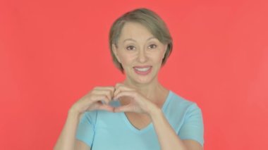 Senior Old Woman showing Heart Shape by Hands on Red Background 
