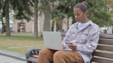 Online Shopping by Excited Young African Woman while Sitting Outdoor on Bench