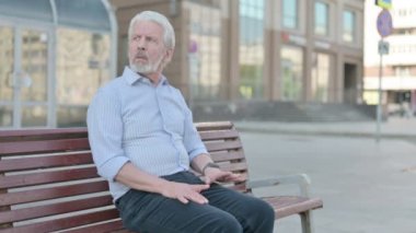 Senior Old Man Browsing Internet on Smartphone while Sitting Outdoor on Bench