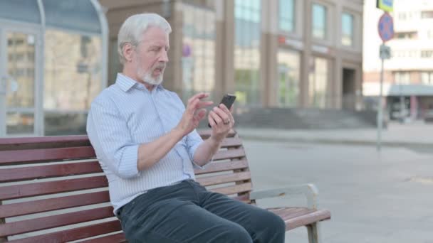 Senior Old Man Celebrating Online Success Smartphone While Sitting Outdoor — Vídeo de Stock
