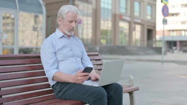 Senior Old Man Using Smartphone Laptop While Sitting Outdoor Bench — ストック動画