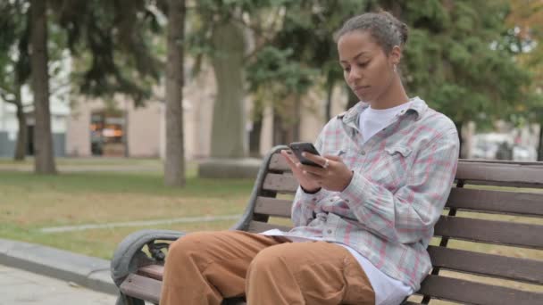 Young African Woman Celebrating Success Smartphone While Sitting Outdoor Bench — Stock videók
