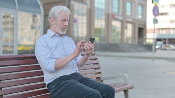 Senior Old Man Browsing Internet Smartphone While Sitting Outdoor Bench — Stockvideo