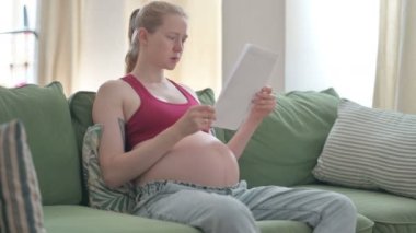 Pregnant Young Woman Reading Documents while Sitting on Sofa