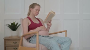 Pregnant Young Woman Reading Book while Stoking Her Big Belly