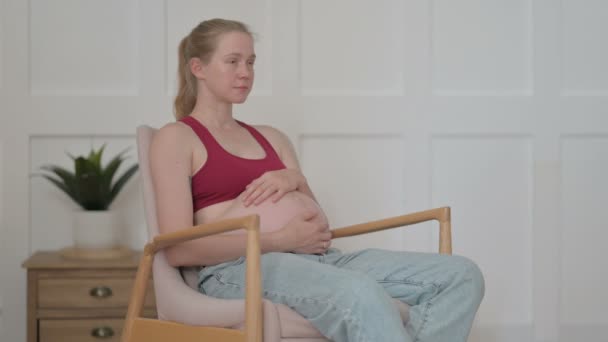 Κάθεται Έγκυος Νεαρή Γυναίκα Κοιτάζοντας Κάμερα Ενώ Χαϊδεύοντας Την Κοιλιά — Αρχείο Βίντεο