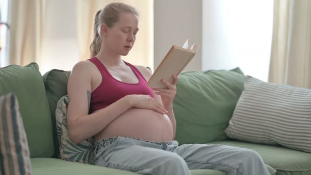 Έγκυος Νεαρή Γυναίκα Ανάγνωση Βιβλίο Ενώ Κάθεται Στον Καναπέ — Αρχείο Βίντεο