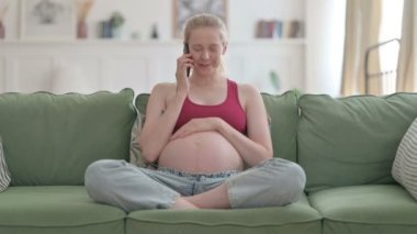 Pregnant Young Woman Talking on Phone while Relaxing on Sofa