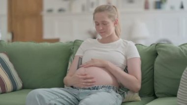 Pregnant Young Woman Stokes, Touches Her Big Belly while Sitting on Sofa