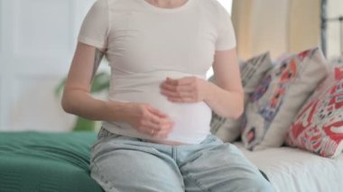 Pregnant Young Woman Stokes Her Big Belly after Removing Shirt, Close Up
