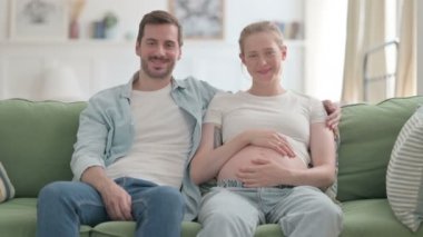 Pregnant Young Woman with Husband Smiling while Holding Her Tummy